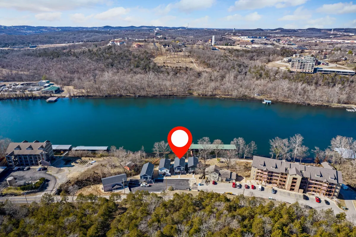 A wide view of the river with surrounding trees, nearby buildings, a road, and a parking area. The natural landscape merges with signs of Branson’s lively community, capturing both the tranquil water and hints of nightlife and entertainment in the area.