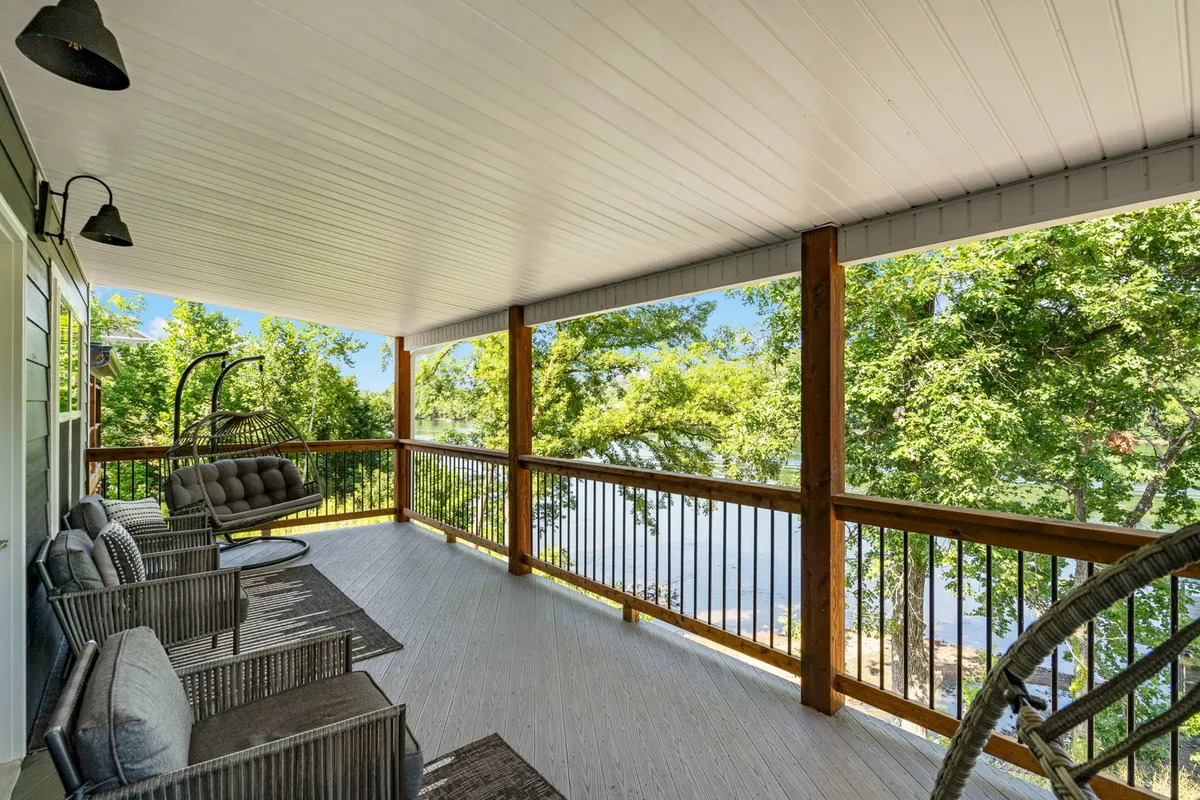 An exterior deck area with a hanging swing chair and rocking chairs, offering a scenic view over the lake and surrounded by green trees. The tranquil setting is perfect for sunrise or sunset moments, connecting the indoor fun space to outdoor relaxation.