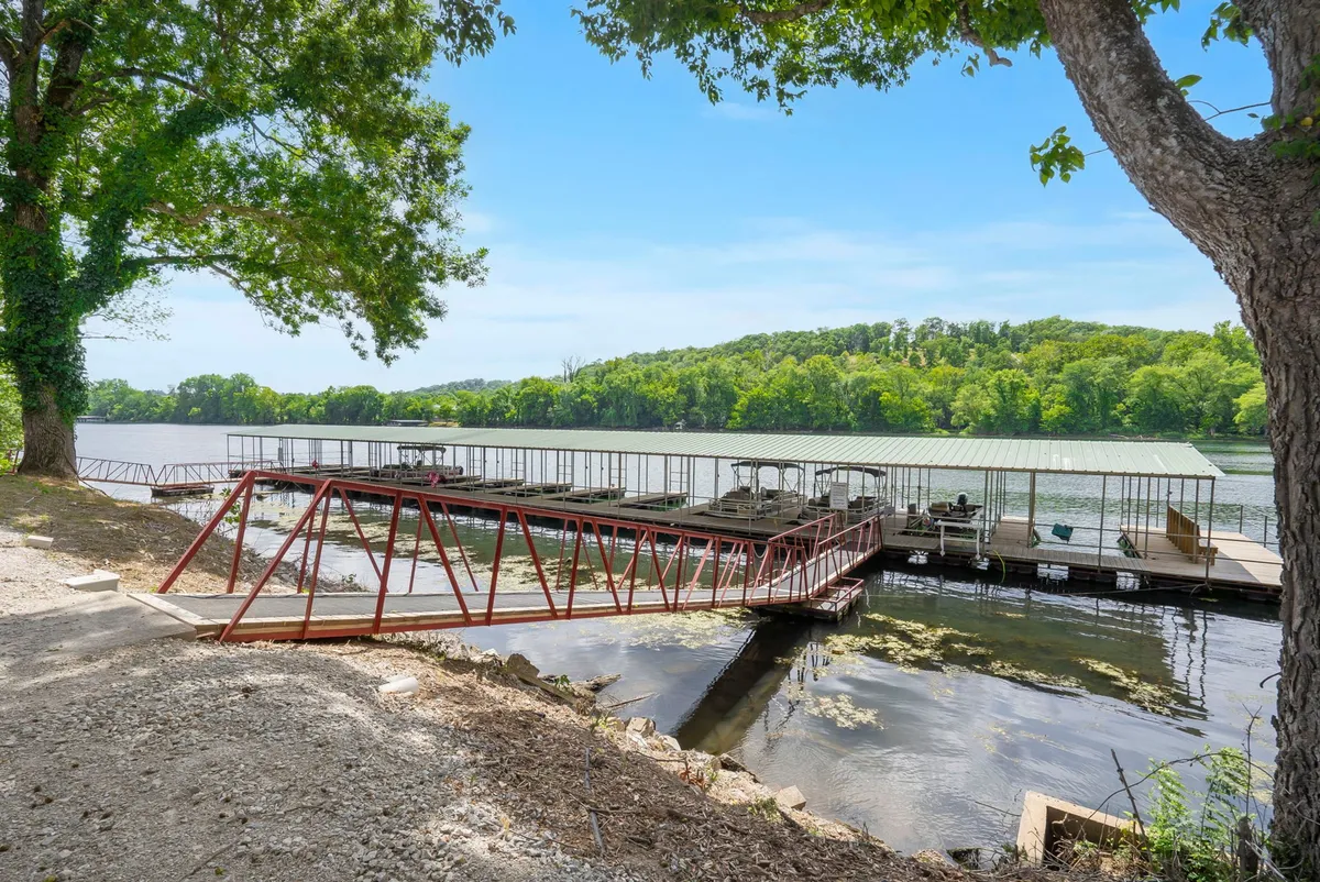 A tranquil lakeside scene featuring a dock stretching out over calm water, surrounded by lush trees and distant hills. The setting invites guests to engage in boating, fishing, or simply relaxing by the lake, all under a serene atmosphere.