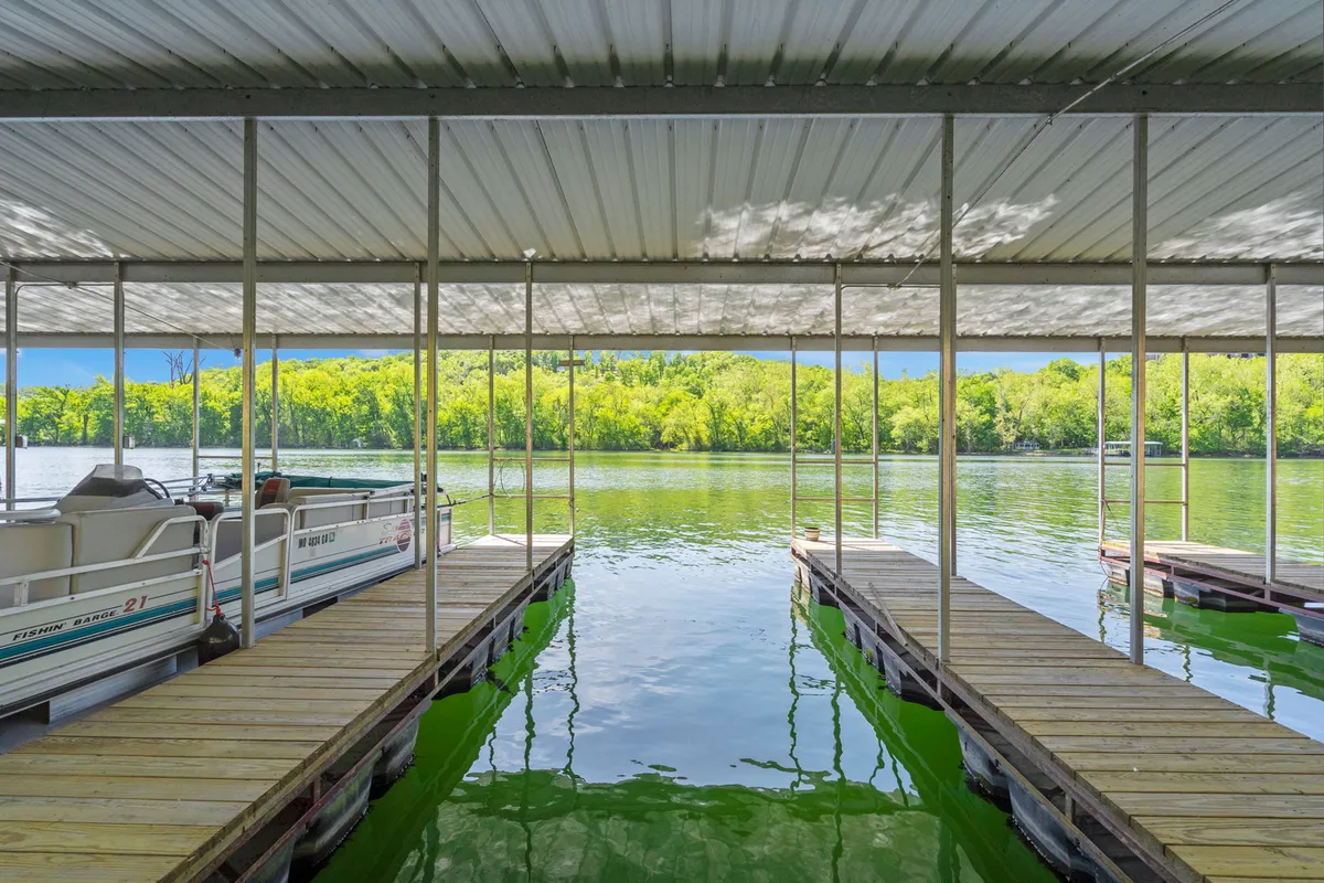 A tranquil scene of boat docks stretching into calm blue water, bordered by lush greenery. The open space around the docks is ideal for walking, relaxing, and enjoying the natural beauty of the lakeside setting.