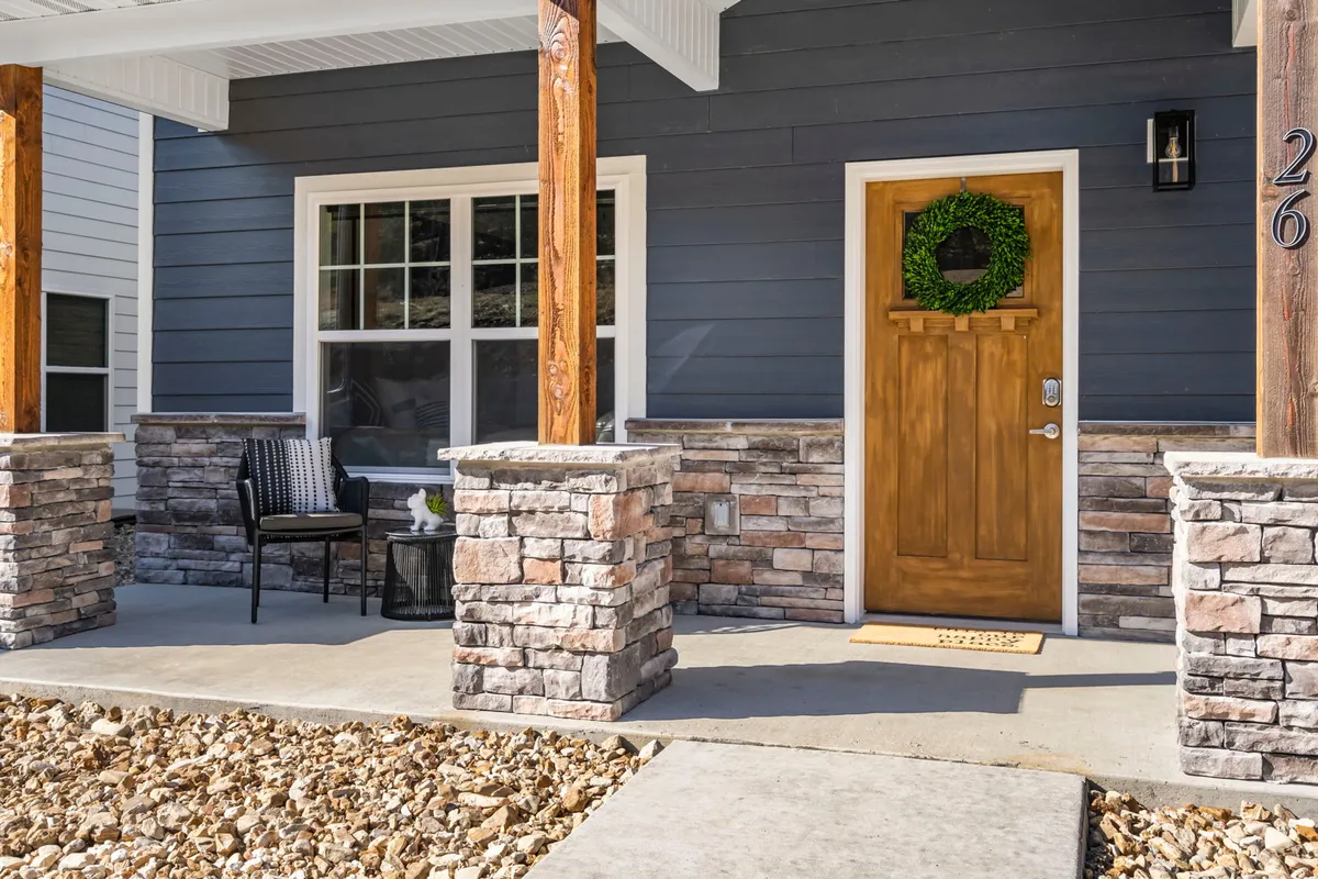 A welcoming front porch with a wooden door adorned by a wreath, flanked by stone pillars and cozy seating. The inviting entrance sets a friendly tone for guests and their pets, making everyone feel at home.