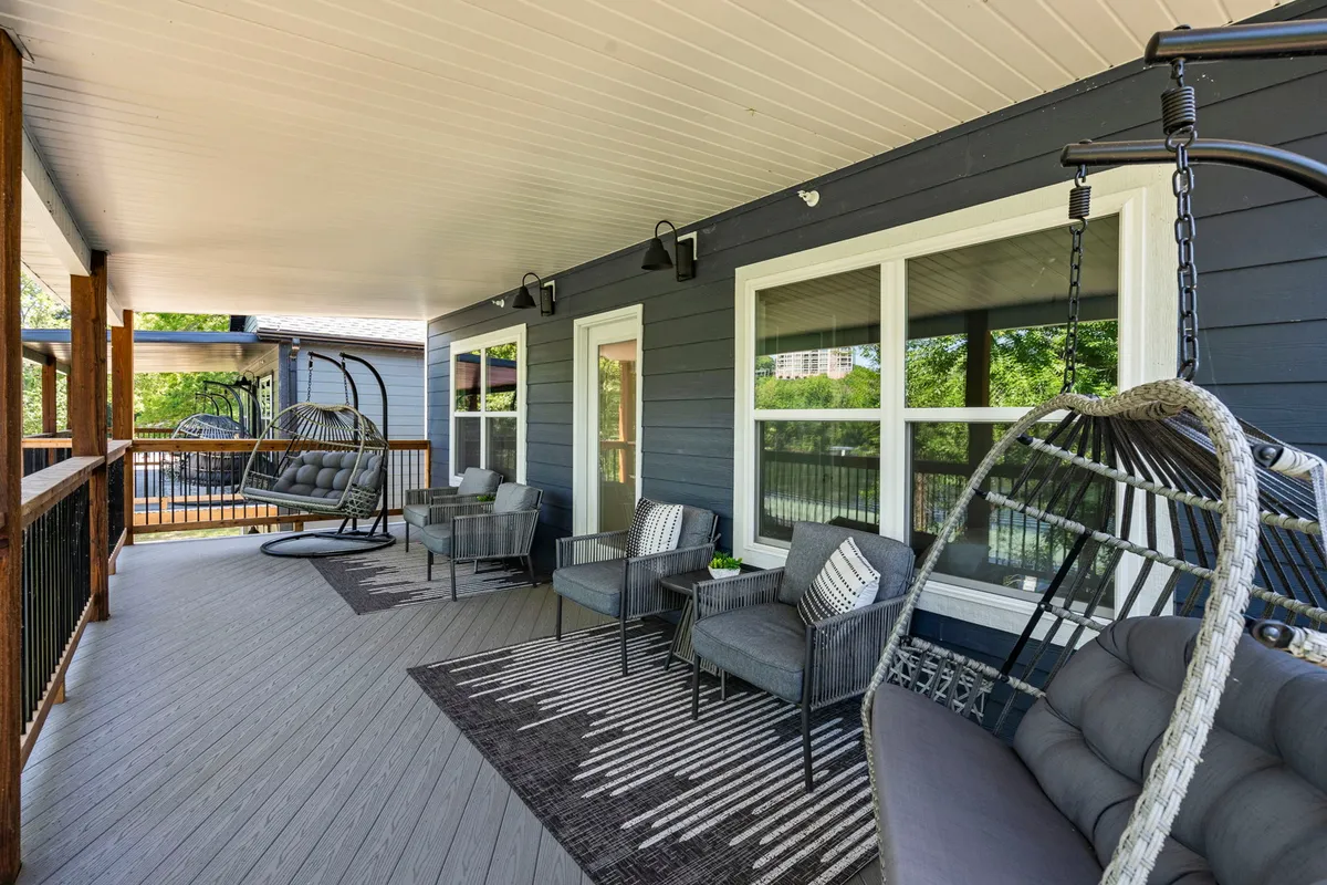 A cozy exterior seating area with hanging chairs and a decorative rug, framed by lush greenery. The spot overlooks the outdoors, making it a perfect place for relaxing, reading, or enjoying meals with family while soaking in the lakeside atmosphere.