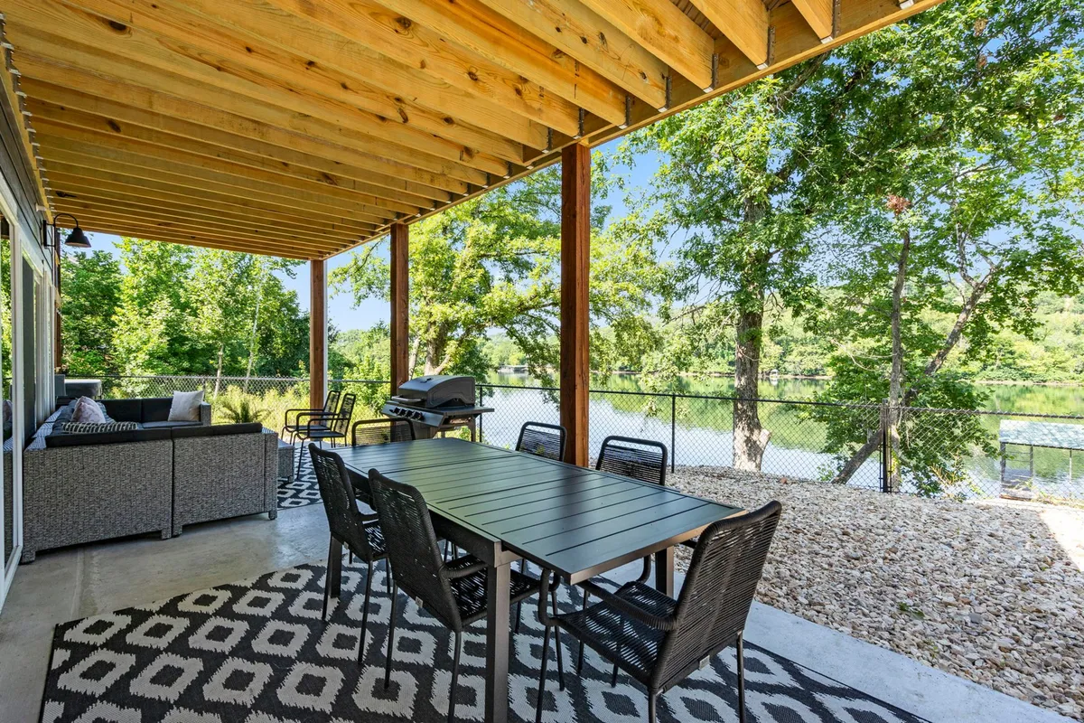 A spacious outdoor patio featuring a large dining table, comfortable seating, a grill, and a panoramic water view. Surrounded by greenery, this area is designed for al fresco meals, celebrations, and enjoying nature's beauty.