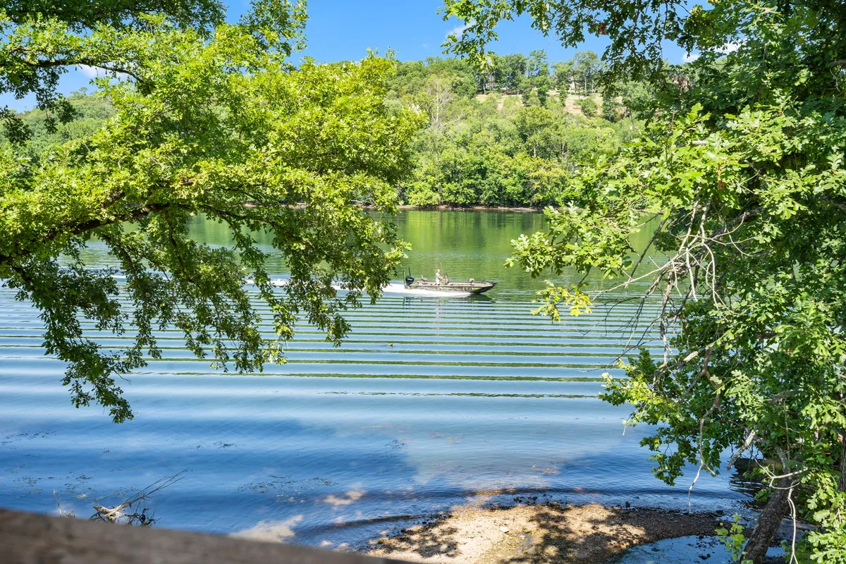 A serene view of calm lake water with a fishing boat and lush greenery along the shore. The tranquil atmosphere invites guests to experience nature and outdoor recreation.