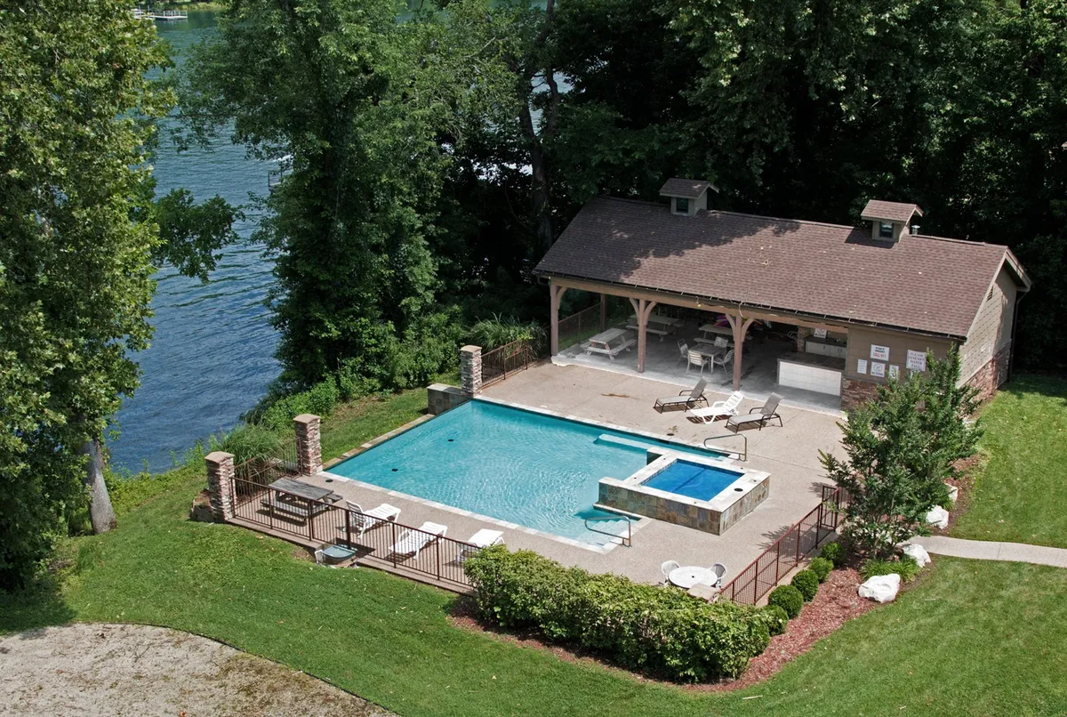 A sparkling outdoor swimming pool surrounded by comfortable lounge chairs, landscaped greenery, and an inviting seating area. The pool area includes views of the lake in the background, creating a serene resort-like setting ideal for relaxing or socializing.